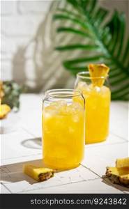 Pineapple cocktail or juice in two glasses with ice on white background with palm leaves. Pineapple cocktail or juice
