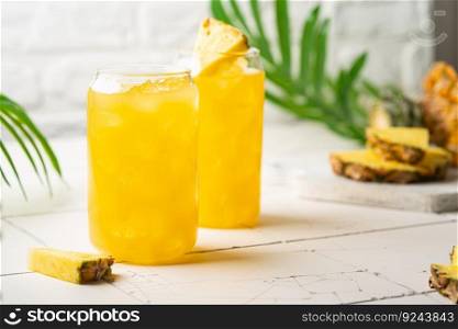 Pineapple cocktail or juice in two glasses with ice on white background with palm leaves. Pineapple cocktail or juice