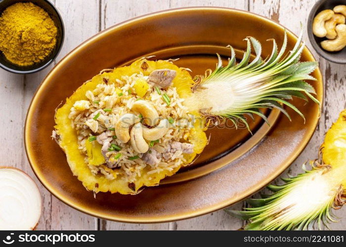 Pineapple Fried Rice with pork, egg, garlic, onion, spring onion, pepper and curry powder, cashew nut on top in oval ceramic plate on old white wood background, top view, Khao Pad Sapparod, Thai food