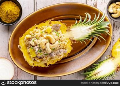 Pineapple Fried Rice with pork, egg, garlic, onion, spring onion, pepper and curry powder, cashew nut on top in oval ceramic plate on old white wood background, top view, Khao Pad Sapparod, Thai food