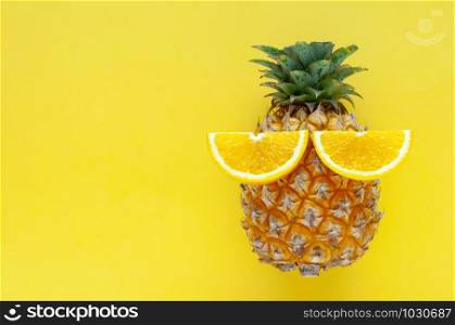 Pineapple fruit with slice oranges set as the eyes isolated on yellow color background for summer time with space for text.