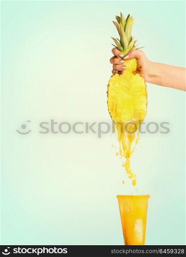 Pineapple juice concept. Female hand holding half of pineapple and presses juice into glass at sunny blue background. Summer beverages splash