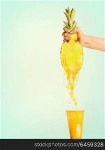 Pineapple juice concept. Female hand holding half of pineapple and presses juice into glass at sunny blue background. Summer beverages splash
