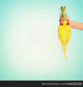 Pineapple juice concept. Female hand holding half of pineapple and presses juice at blue background. Summer beverages splash