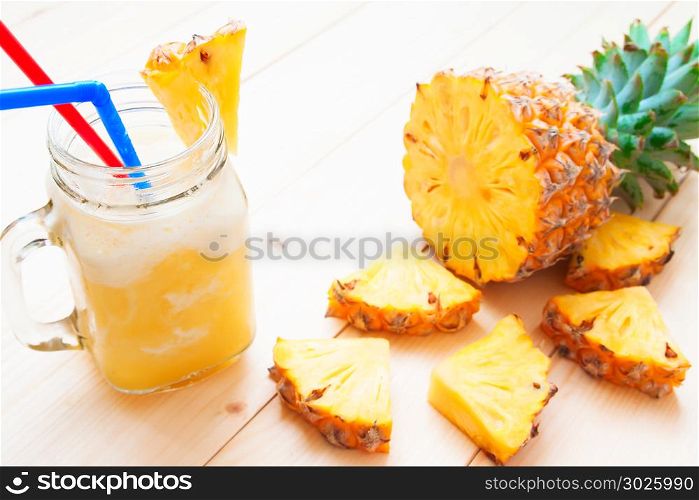 Pineapple smoothie in glass jar and sliced pineapple on wooden table