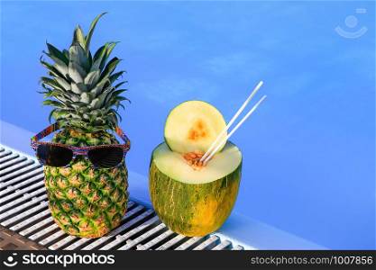 Pineapple wearing sunglasses and melon at blue swimming pool