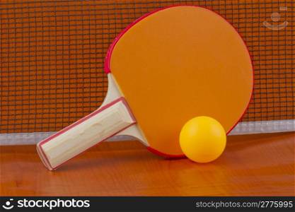 Ping pong orange racket with yellow ball near the net