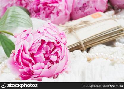 pink a peony on lace. fresh pink peonies with pile of old mail on white lace background