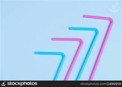 Pink and blue pastel colored drinking cocktail straws on blue paper background with side copy space