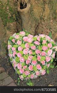 pink and green heart shaped sympathy arrangement near a tree