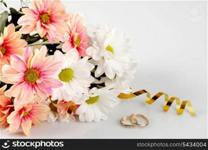 Pink and white daisy with gold ribbon and wedding rings. Still life isolated on white