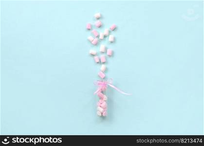 Pink and white marshmallow pieces is sprayed from a small glass container on a pastel blue background. Flat lay minimalism. Top view. Marshmallow is sprayed from a small glass container on a blue background.