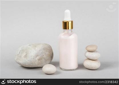 Pink anti-aging collagen, facial serum in transparent glass bottle with gold pipette and natural stones on grey background. Natural Organic Spa Cosmetic Beauty Concept. Front view.. Pink anti-aging collagen, facial serum in transparent glass bottle with gold pipette and natural stones on grey background. Natural Organic Spa Cosmetic Beauty Concept. Front view