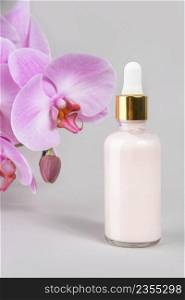 Pink anti-aging collagen, facial serum in transparent glass bottle with gold pipette and natural orchid flower on grey background. Natural Organic Spa Cosmetic Beauty Concept. Front view.. Pink anti-aging collagen, facial serum in transparent glass bottle with gold pipette and natural orchid flower on grey background. Natural Organic Spa Cosmetic Beauty Concept. Front view