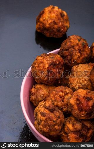 Pink bowl with fried meatballs with spices. Homemade food.