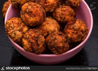 Pink bowl with fried meatballs with spices. Homemade food.