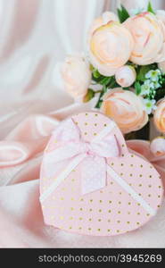 Pink camellias and gift box with bow on a background of the silk fabric; vertical image