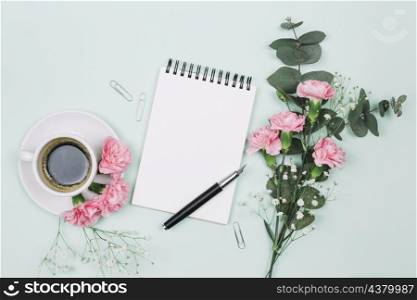 pink carnations gypsophila flowers with coffee cup spiral notepad fountain pen blue backdrop