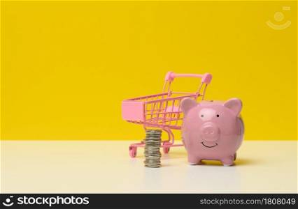 pink ceramic piggy bank and a stack of coins on a white table, yellow background. Savings concept, budget planning. Income growth
