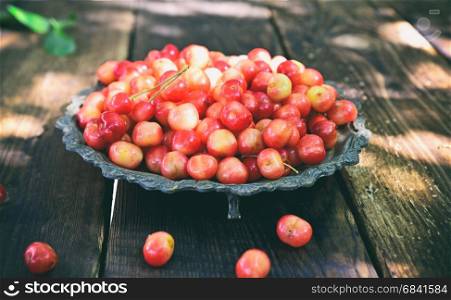 Pink cherry in a metal plate on a wooden table, vintage toning