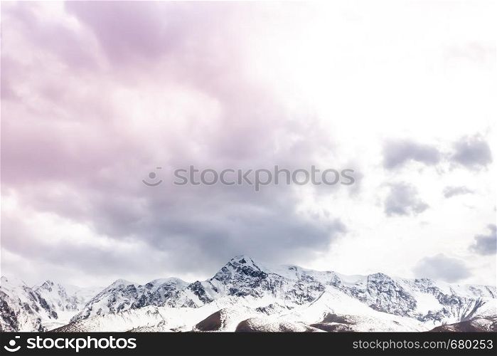 Pink clouds over mountain range. Rocks under snow on horizon. Sunset in mountain valley