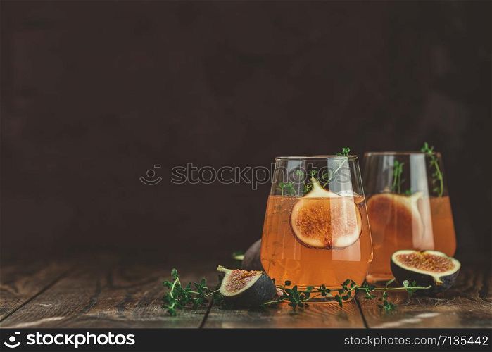 Pink cocktail with fig, thyme and ice in glass on dark wooden background, close up. Summer drinks and alcoholic cocktails. Alcoholic or detox cocktail