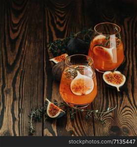 Pink cocktail with fig, thyme and ice in glass on dark wooden background, close up. Summer drinks and alcoholic cocktails. Alcoholic or detox cocktail