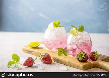 Pink cocktail with lime, crushed ice, strawberries and mint on the light background, selective focus image, copy spice for you text, summer vacation and party concept.