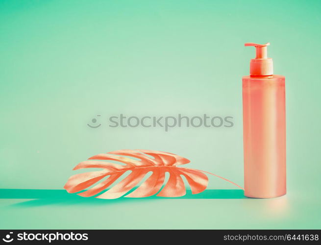 Pink cosmetic bottle with dispenser pump and tropical leaf at mint background. Summer skin care or sunblock product with copy space for design