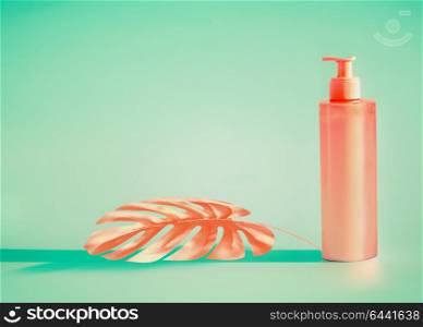Pink cosmetic bottle with dispenser pump and tropical leaf at mint background. Summer skin care or sunblock product with copy space for design