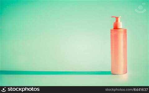 Pink cosmetic bottle with dispenser pump at mint background. Summer skin care lotion or sunblock product with copy space for design