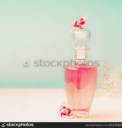 Pink Cosmetic bottle with skin care product or perfume with flowers Stands on the table at turquoise background, front view. Beauty concept