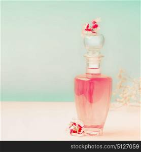 Pink Cosmetic bottle with skin care product or perfume with flowers Stands on the table at turquoise background, front view. Beauty concept