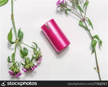 Pink cosmetic product on white background with pink flowers. Top view. Natural cosmetic.
