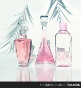 Pink cosmetic products bottles in sunlight with palm leaves shadow at white background. Modern facial skin care. Beauty anti aging concept