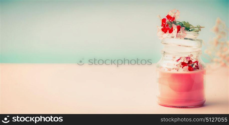 Pink cream in glass jar for skin care with flowers Stands on the table at turquoise background, front view, banner. Beauty, cosmetic, spa or body care concept