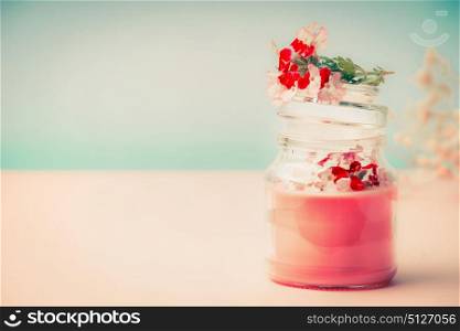 Pink cream in glass jar for skin care with flowers Stands on the table at turquoise background, front view. Beauty, cosmetic, spa or body care concept