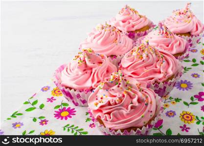 Pink cupcakes on floral napkin. Birthday cupcake with whipped cream. Homemade cupcakes served for party. Birthday background.. Pink cupcakes on floral napkin