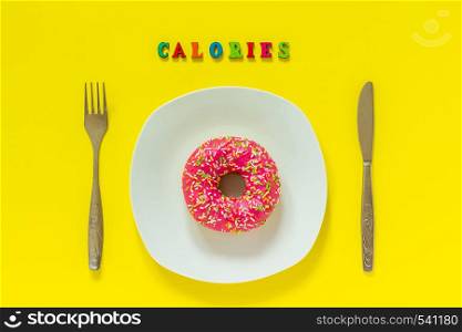 Pink donut on white plate and cutlery table knife fork Text Calories. Still life on yellow background. Top view Flat lay Concept No Diet day. Calories and Pink donut on white plate and knife fork on yellow background.