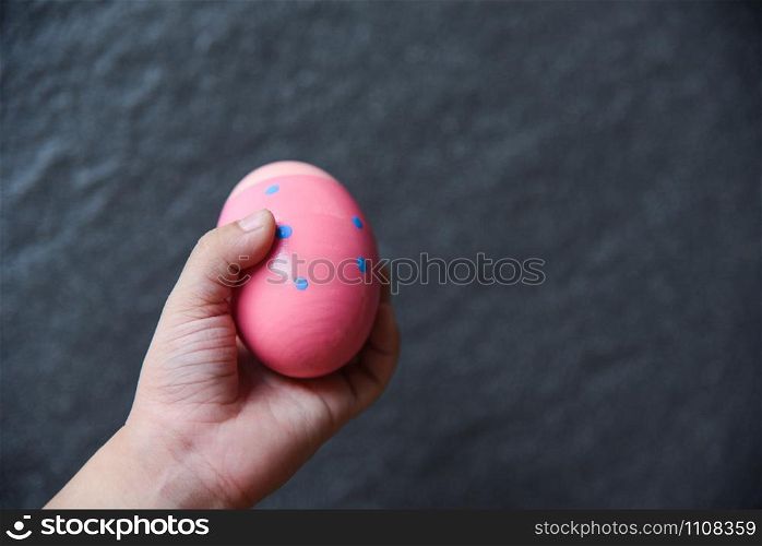 Pink easter egg hunt in Kids hand on dark background
