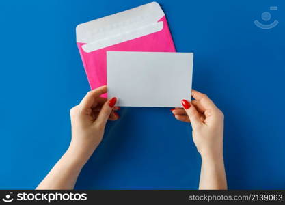 Pink envelope with a blank card in hands on a blue background. Hands holding a pink envelope with a blank letter on a blue background.. Pink envelope with a blank card in hands on a blue background.