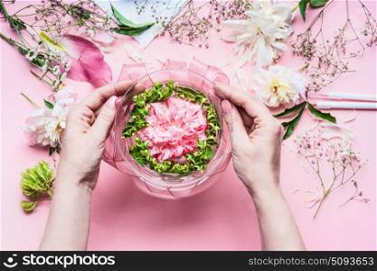 Pink Florist workspace with Lilies and other flowers, glass vase with water. Female hands making Festive Flowers arrangements , top view