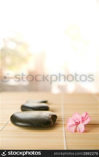 pink flower with black stones over biege bamboo. Shallow DOF.