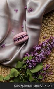 pink french macaroon or macaron cookie and a lilac flowers on a cloth and straw stand background. Natural fruit and berry flavors, creamy stuffing.. pink french macaroon or macaron cookie and a lilac flowers on a cloth and straw stand background. Natural fruit and berry flavors, creamy stuffing