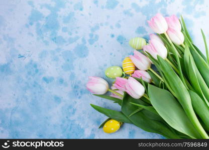 Pink fresh tulips with easter eggs on blue background with copy space, top view. Pink fresh tulips