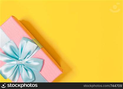 Pink gift box tied with blue ribbon with bow at the top on yellow background. Copy space for text. Minimal flat lay. Top view. Birthday, New year, Mother?s day, Women?s day celebration concept.