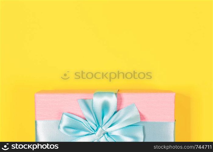 Pink gift box tied with blue ribbon with bow at the top on yellow background. Copy space for text. Minimal flat lay. Top view. Birthday, New year, Mother?s day, Women?s day celebration concept