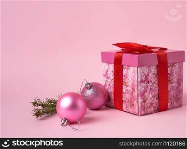 pink gift box with bow, green spruce branch and two decorative pink balls on a pink background