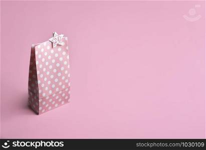 Pink gift paper bag with white dots and number 24, on a pink background. Christmas advent calendar concept. Christmas Eve context. Gifting theme.