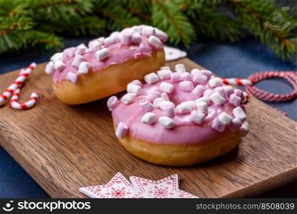 Pink glazed doughnut and marshmallow with Christmas decorations on a wooden cutting board against a dark concrete background. Pink glazed doughnut and marshmallow with Christmas decorations on a wooden cutting board